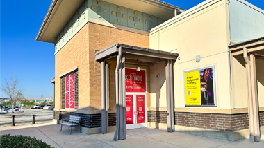 Exterior of a hiring center building with red “Now Hiring” signage on the entrance doors and posters on the windows.